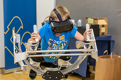 Lange Nacht der Forschung in Hagenberg: Kind mit VR Brille "schwebt" auf einem Gerät ©Erwin Pils