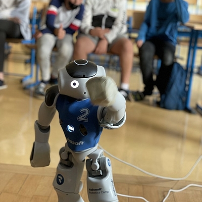  Ein kleiner Roboter mit großen Augen schaut in die Kamera und hebt den linken Arm zur Begrüßung ©Michael Kirchberger