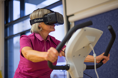 Dame sitzt am Ergometer und hat VR-Brille auf