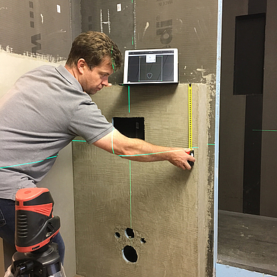 Mann vermisst Wand mit digitalem Rollmeter, welches die Vermessungen (Linien) auf die Wand projeziert