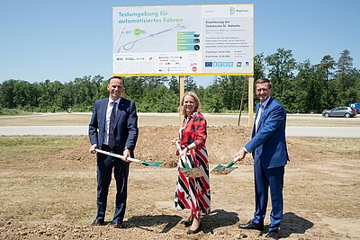 Spatenstich für neue Testregion für automatisiertes Fahren in St. Valentin © Land OÖ/ Liedl Jochen Danninger, Eva Tatschl-Unterberger und Markus Achleitner vor einer Schautafel mit jeweils einer Schaufel in der Hand.Foto: Land OÖ/ Liedl